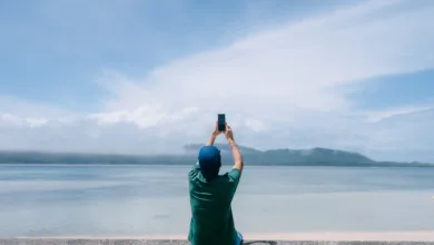 Seyahat fotoğrafçılığı için hangi mobil aksesuarlar iyidir? 30 person sits on wall in front of water while holiding up their phone